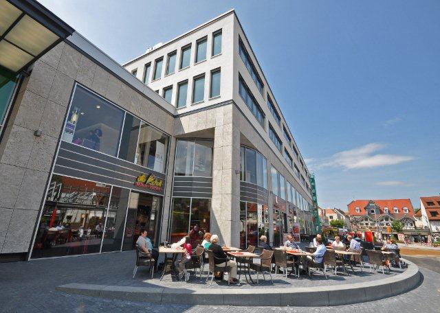 Einkaufsgalerie von außen mit Bänken und Tische wo Menschen sitzen