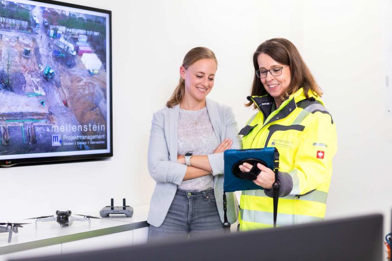 Zwei Frauen stehen nebeneinander und gucken sich etwas auf einem Tablet an