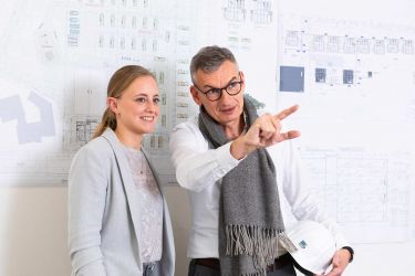 Zwei Menschen stehen vor Bauplänen und sprechen miteiandner