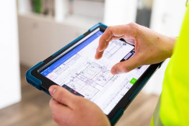 Mensch hält ein Tablet auf dem Bauplänen abgebildet sind