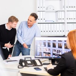 3 Menschen sind an einem Schreibtisch und unterhalten sich